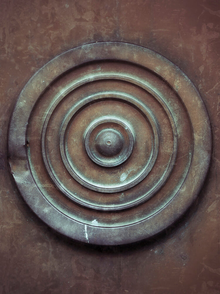 koppar-dorr-detalj-cirkel-skogskyrkogarden Närbild av dörrdetalj i koppar med cirkulärt mönster och grön patina.