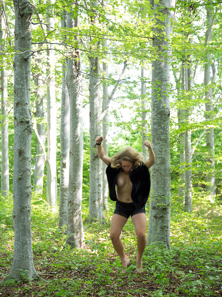 vild-kvinna-hoppar-skog-raw-fotokonst Kvinna i rörelse som hoppar från ett träd i skogen iklädd päls i ett rått och vilt uttryck.