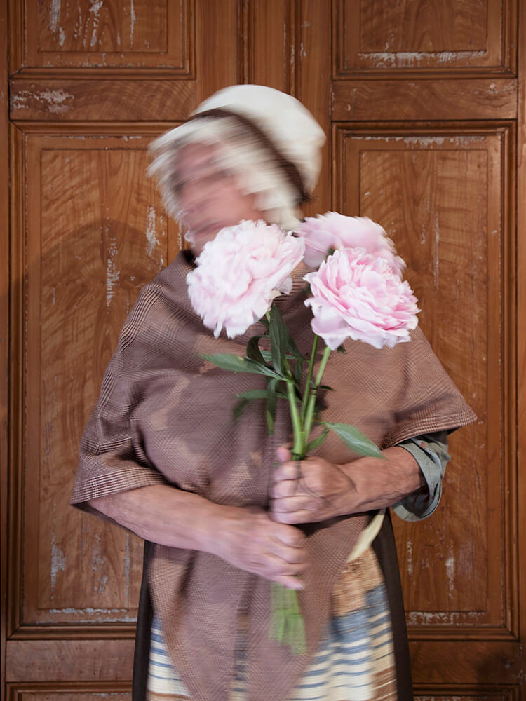 wira-kvinnor-pioner-ansikte-viktoria-davidsson Kvinna i tidstypiska kläder från tidigt 1900-tal håller i rosa pioner.