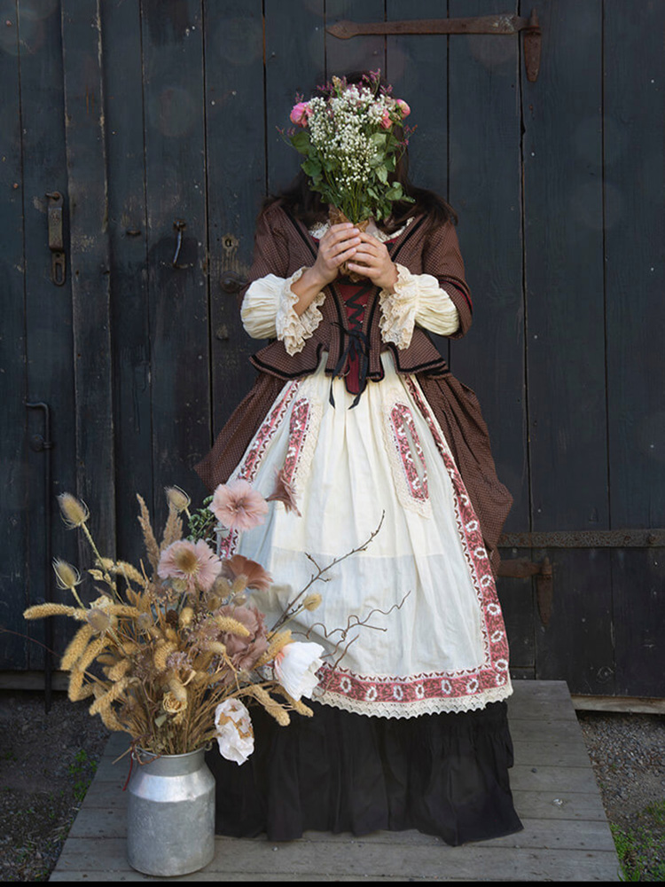 wiras-kvinnor-lider-blommor-dörr-viktoria-davidsson Kvinna i tidstypiska kläder står framför en svart dörr till ett lider och håller en blombukett framför ansiktet.